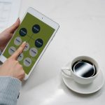 Hands holding a tablet with a diagram, next to a cup of black coffee on a desk, symbolizing modern work life.